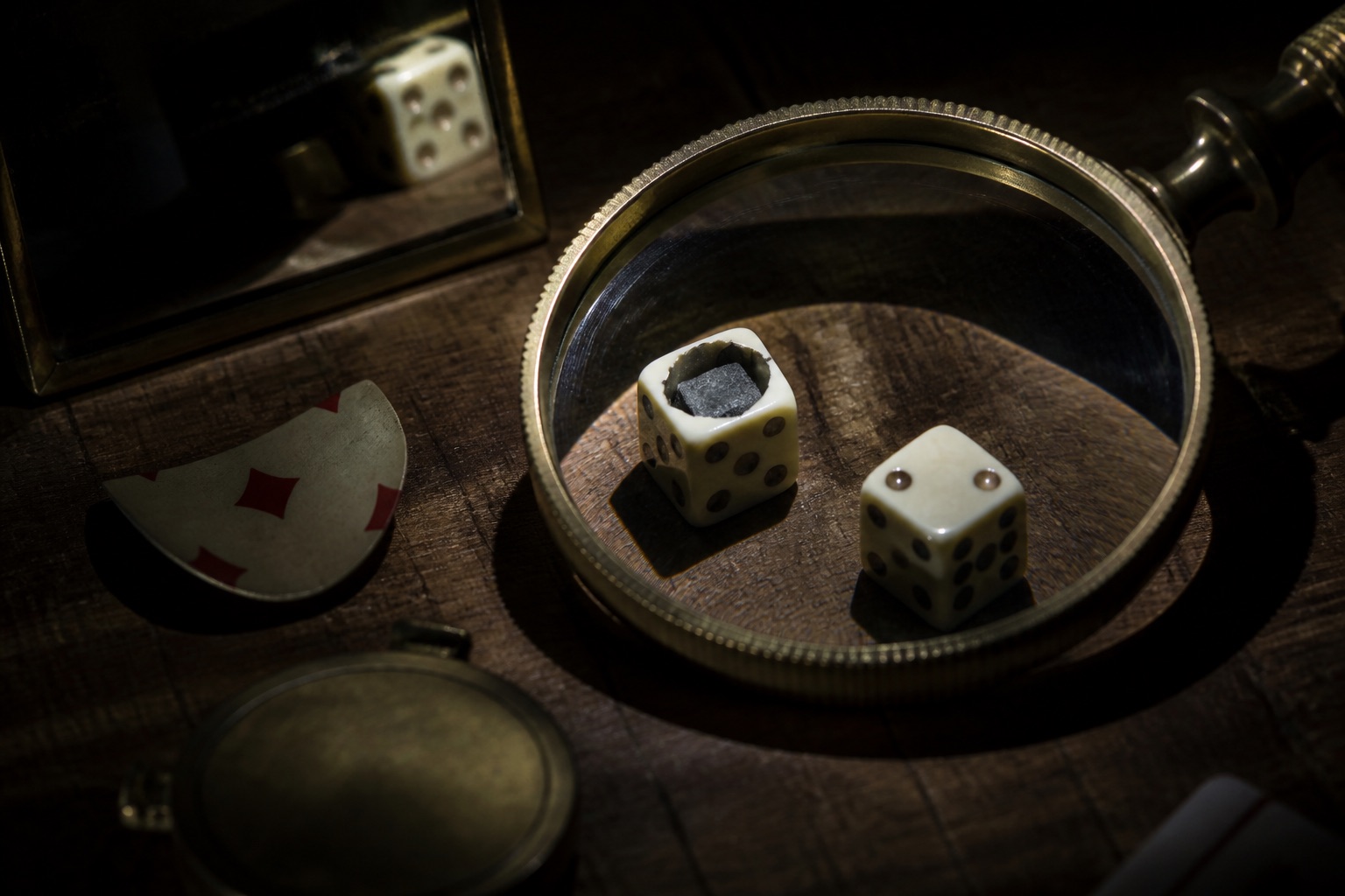 Dice cut open to reveal a lead weight, under a brass magnifying glass in hard spotlight